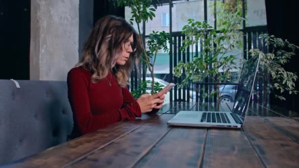 Frau sitzt mit Telefon und Computer am Tisch — Stockvideo