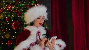 Mutlu kadın Bayan Noel Baba, Noel ofisinde telefonda konuşuyor. Karantinada tatiller. Uzaktan iletişim, tatil hediyeleri ve indirimler.