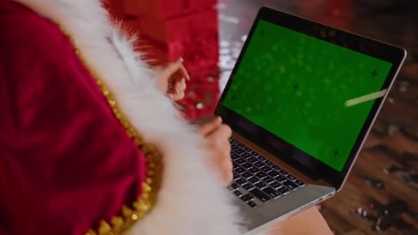 In ihrem Weihnachtsbüro kommuniziert die fröhliche Frau Weihnachtsmann auf dem Laptop. Urlaub in Quarantäne. Fernkommunikation, Weihnachtsgeschenke und Rabatte. — Stockvideo