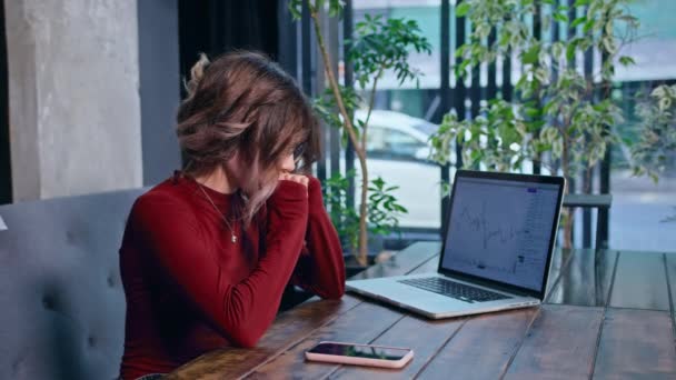 Жінка сидить з телефоном і комп'ютером за столом — стокове відео
