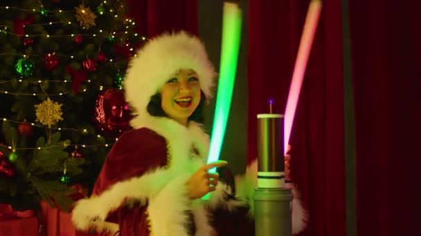 Šťastná žena v kostýmu Santa si hraje s neonovými trubicemi u cívky tesla, na pozadí vánočního stromku. Novoroční show, dětská dovolená. — Stock video