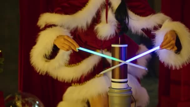 Happy woman in santa costume plays with neon tubes near the tesla coil, against the background of the Christmas tree. New Years show, childrens holiday. — Stock Video
