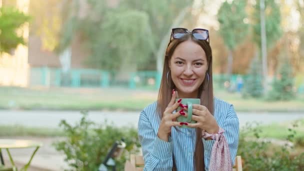 Relajado sonriente mujer satisfecha con la taza roja de café de pie en el extremo de la calle disfrutando de un día soleado — Vídeo de stock