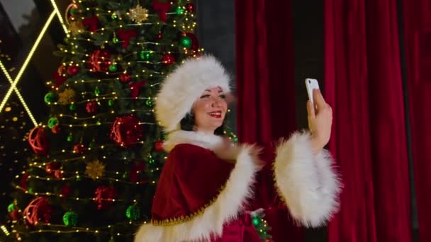 Szczęśliwa kobieta pani Mikołajowa rozmawia przez telefon w swoim świątecznym biurze. wakacje w kwarantannie. komunikacja zdalna, prezenty wakacyjne i zniżki. — Wideo stockowe
