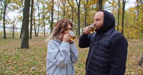 Cara feliz e jovem bebem chá na floresta no outono, caminham na floresta. — Vídeo de Stock