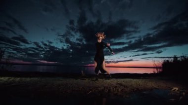 Cadılar Bayramı kostümü içinde mutlu genç bir kadın gün batımında doğada dans ediyor, mistik görüntüler..