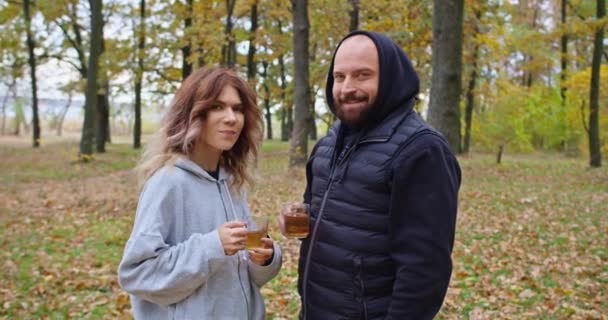 Cara feliz e jovem bebem chá na floresta no outono, caminham na floresta. — Vídeo de Stock