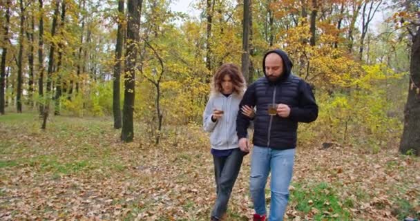 Cara feliz e jovem bebem chá na floresta no outono, caminham na floresta. — Vídeo de Stock