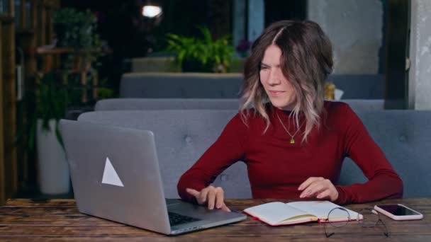 Kvinna sitter vid ett bord med en bärbar dator och gläds — Stockvideo