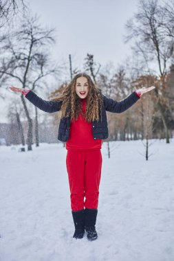 Genç ve mutlu bir kadın kış parkında eğleniyor, kar atıyor, elleri soğuk, salınımlar ölçüsüz..
