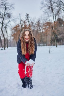 Genç ve mutlu bir kadın kış parkında eğleniyor, kar atıyor, elleri soğuk, salınımlar ölçüsüz..