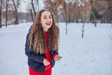 Genç ve mutlu bir kadın kış parkında eğleniyor, kar atıyor, elleri soğuk, salınımlar ölçüsüz..