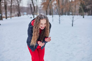 Genç ve mutlu bir kadın kış parkında eğleniyor, kar atıyor, elleri soğuk, salınımlar ölçüsüz..
