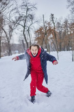 Genç ve mutlu bir adam kış parkında eğleniyor, kar atıyor, elleri soğuk, salınımlar ölçüsüz..