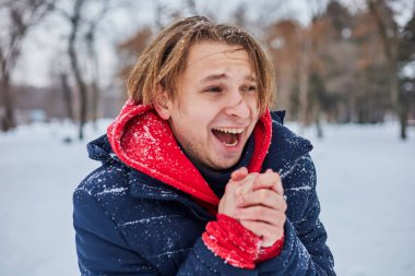 Genç ve mutlu bir adam kış parkında eğleniyor, kar atıyor, elleri soğuk, salınımlar ölçüsüz..