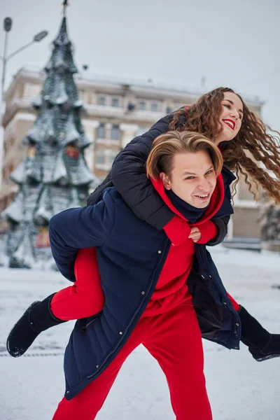 Jonge familieman en meisje brengen de dag door in het park op een besneeuwde dag. Emotioneel jong paar dat plezier heeft tijdens het wandelen in de winterstad, een levendige man knuffelt zijn lachende mooie vrouw. — Stockfoto