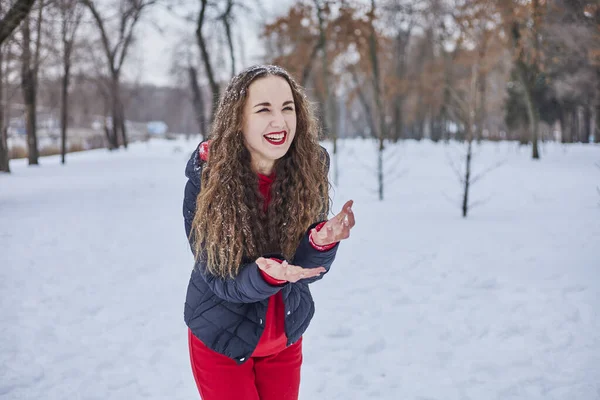 A young happy woman is having fun in a winter park, throwing snow, it is cold in her hands, the emissions are off scale. — Stock Photo, Image