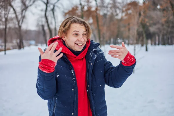 stock image a young happy man is having fun in a winter park, throwing snow, it is cold in his hands, the emissions are off scale.