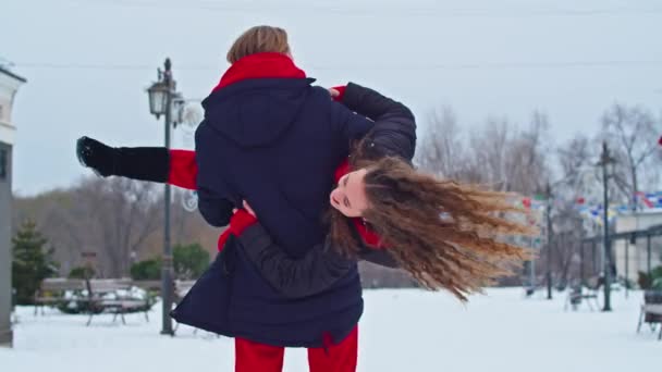 Jovem cara de família e menina passar o dia no parque em um dia nevado. Jovem casal emocional se divertindo enquanto caminha na cidade de inverno, um homem animado abraça sua bela mulher rindo. — Vídeo de Stock