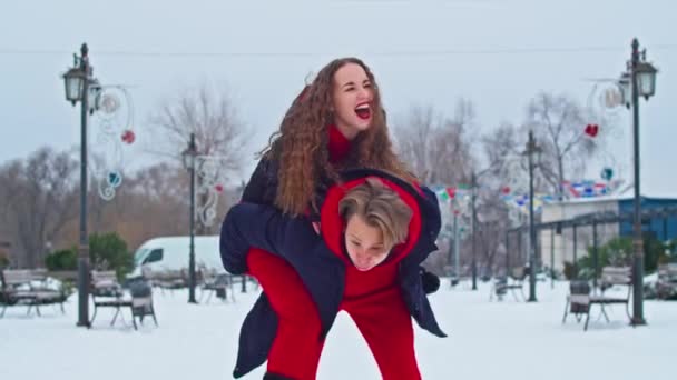 Krivoy Rog, Ukraine - 01.01.22 young family guy and girl spend the day in the park on a snowy day. Emotional young couple having fun while walking in the winter city, a lively man hugs his laughing — Stockvideo