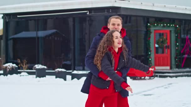 Jonge familieman en meisje brengen de dag door in het park op een besneeuwde dag. Emotioneel jong paar dat plezier heeft tijdens het wandelen in de winterstad, een levendige man knuffelt zijn lachende mooie vrouw. — Stockvideo