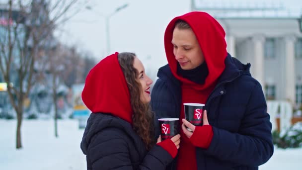 Krivoy Rog, Ukraine - 01.01.22 young family guy and girl spend the day in the park on a snowy day. the guy hugs the girl while standing on the street, they drink coffee together. — Vídeo de Stock