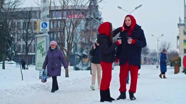 Krivoy Rog, Ukraine - 01.01.22 young family guy and girl spend the day in the park on a snowy day. the guy hugs the girl while standing on the street, they drink coffee together. — Vídeo de Stock