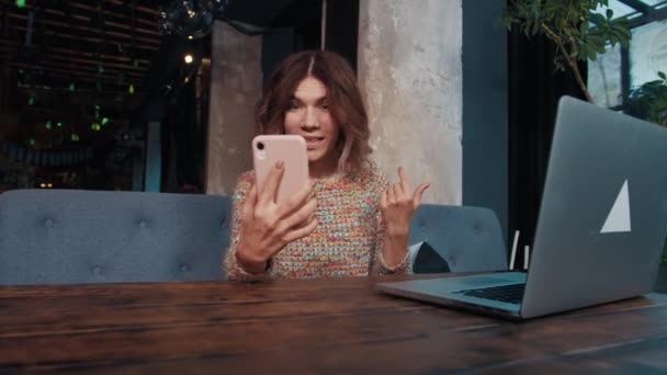 Счастливая девушка блоггер разговаривает по телефону, сидя в кафе — стоковое видео