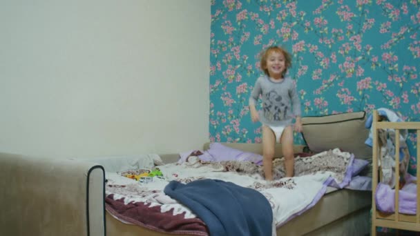 一个快乐的小男孩在家里跳上了床，和他的父亲一起玩球，父亲把球扔到他的屏幕外. — 图库视频影像