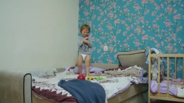 Küçük mutlu bir çocuk evde yatağa atlıyor ve babasıyla top oynuyor. Babası topu ekranın dışına atıyor..