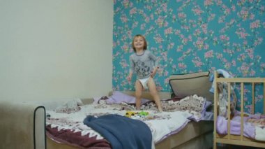 Küçük mutlu bir çocuk evde yatağa atlıyor ve babasıyla top oynuyor. Babası topu ekranın dışına atıyor..