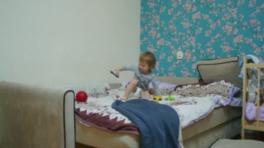 Küçük mutlu bir çocuk evde yatağa atlıyor ve babasıyla top oynuyor. Babası topu ekranın dışına atıyor..