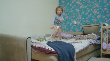 Küçük mutlu bir çocuk evde yatağa atlıyor ve babasıyla top oynuyor. Babası topu ekranın dışına atıyor..