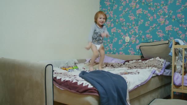 Ein kleines glückliches Kind springt zu Hause auf das Bett und spielt mit seinem Vater Ball, der Vater wirft ihm den Ball aus dem Off zu. — Stockvideo