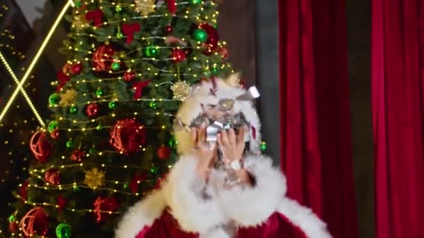 Feliz mujer señora santa arrojar encima de papel de brillo en el fondo del árbol de Navidad. — Vídeo de stock