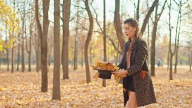 Sonbahar parkında ceketli, şapkalı ve atkılı mutlu bir kadın.