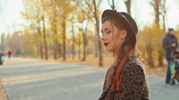 Счастливая игривая женщина в пальто, шляпе и шарфе в осеннем парке — стоковое видео