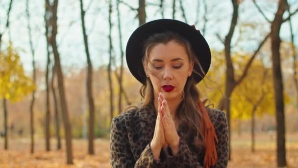 Smutna kobieta w płaszczu i kapeluszu w jesiennym parku próbuje ogrzać ręce, — Wideo stockowe