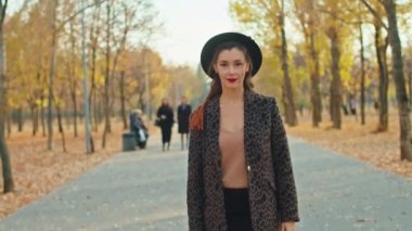 Sonbahar parkında ceketli, şapkalı ve atkılı mutlu bir kadın.