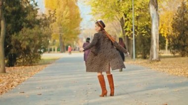 Sonbahar parkında ceketli, şapkalı ve atkılı mutlu bir kadın.