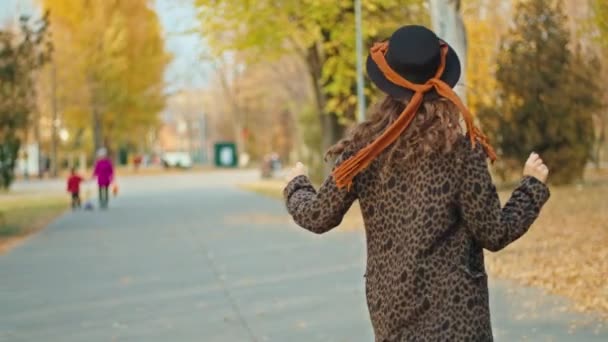 가을 파크에서 코트를 입고 모자를 쓰고 스카프를 두른 행복 한 여성 — 비디오