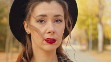 Sonbahar parkında paltolu ve şapkalı üzgün kadın etrafına bakıyor.