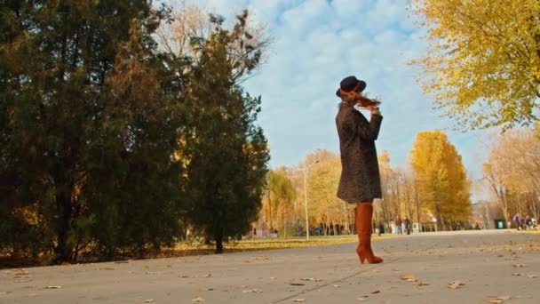 Glückliche verspielte Frau in Mantel, Mütze und Schal im Herbstpark filmt sich mit dem Handy beim Fotografieren. — Stockvideo
