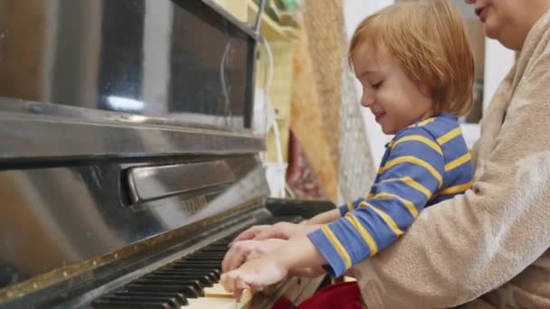 Mały szczęśliwy 2-letni dzieciak uczy się grać na pianinie w domu z babcią. — Wideo stockowe