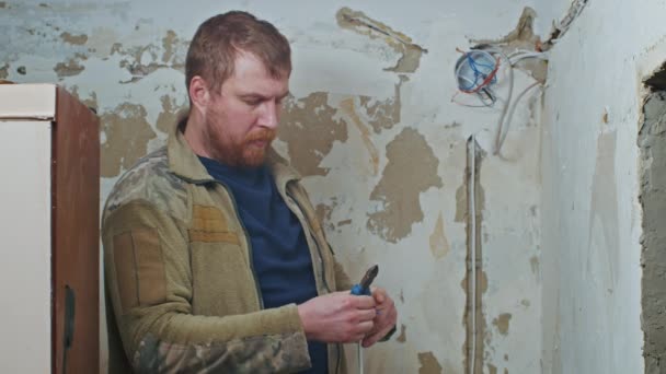 A male electrician performs installation work in an apartment before renovation. — Stock Video