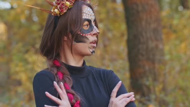 Mladá žena se Santa Muerte make-up oblečená v černých šatech smrti kráčí na pozadí podzimního listí v lese při západu slunce. Day of the Dead nebo Halloween koncept. — Stock video