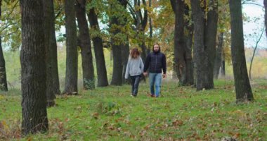 Sonbahar ormanlarında mutlu genç bir çift yol boyunca yürüyor..