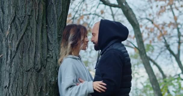 Heureux jeune couple dans la forêt d'automne montrer leurs sentiments, le gars étreint la fille par l'arbre. — Video