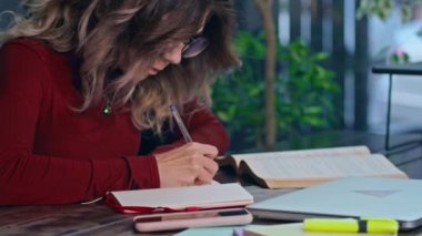 Genç, üzgün, ev ödevlerinden bunalmış bir kız öğrenci bir kafede dizüstü bilgisayarla oturuyor..