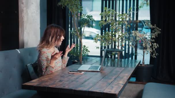 Счастливая блоггерша разговаривает на ноутбуке сидя в кафе — стоковое видео